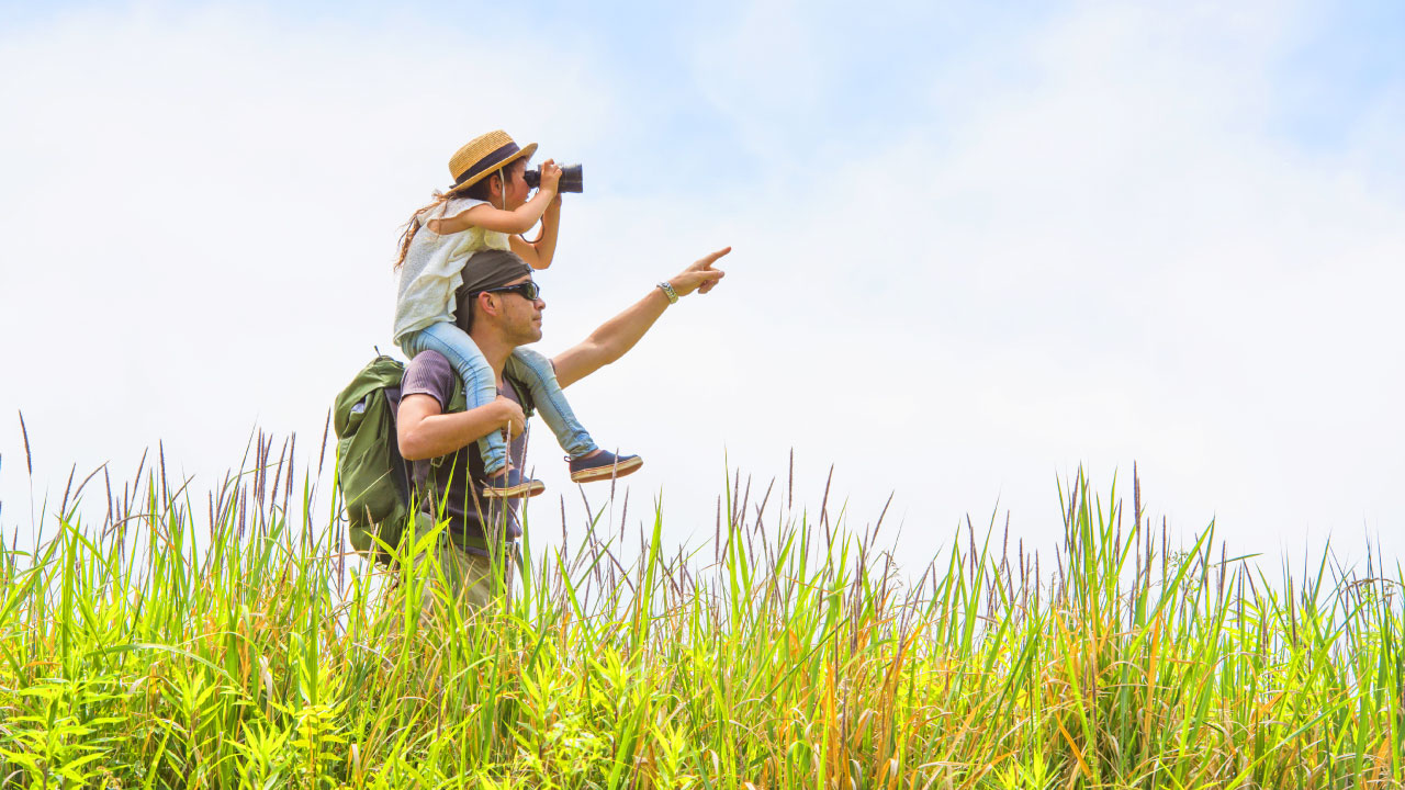 man holding daughter while she looks through binoculars for eye health
