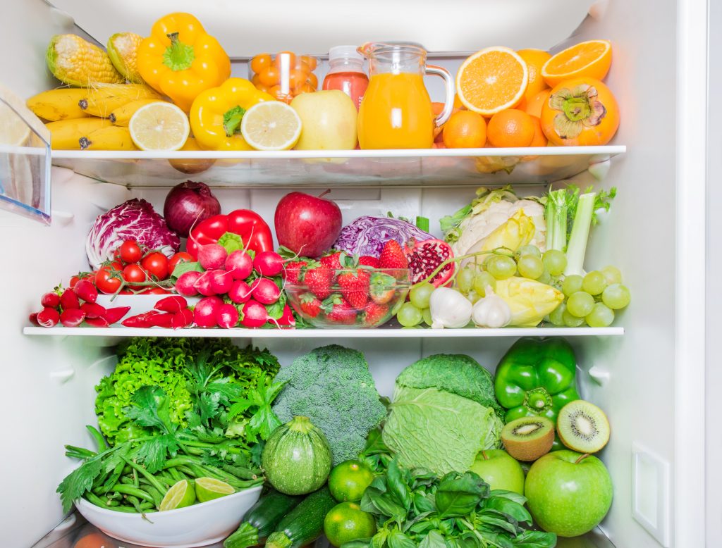 Colorful assortment of fresh fruits and vegetables arranged on refrigerator shelves